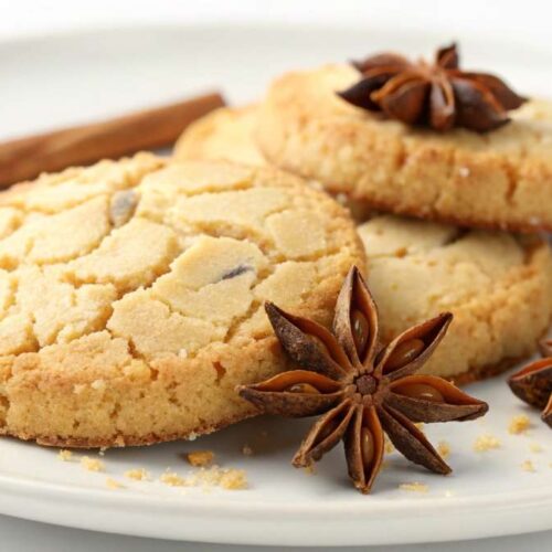 Freshly baked anise cookies on a white plate with whole star anise and cinnamon stick